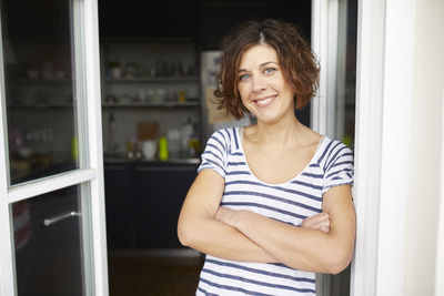 Portrait of content mature woman leaning against open balcony door