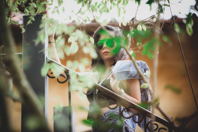 Portrait of young woman holding wearing sunglasses standing against railing