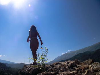 Rear view of woman standing on mountain against blue sky during sunny day