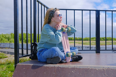 A young girl of 16-18 years old sits on a ramp in a skate park