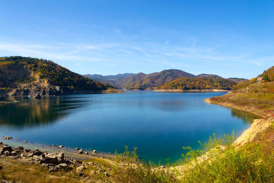 Scenic view of lake by mountains against blue sky