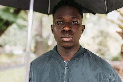 Young african american man under black umbrella in rain, sad. fall or spring weather