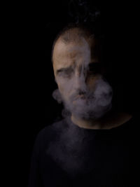 Portrait of man smoking cigarette against black background