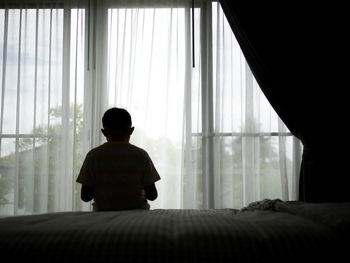 Rear view of boy sitting on bed at home