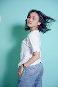 Portrait of young woman standing against blue background