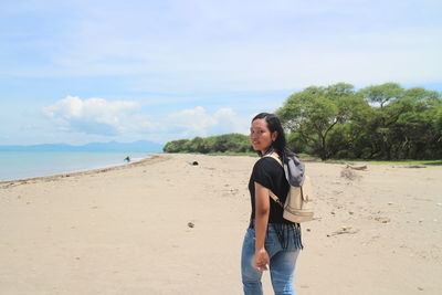 Young woman standing on beach against sky