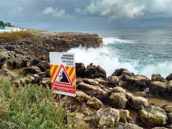 Information sign on rock by sea against sky