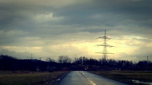 Road passing through field against cloudy sky