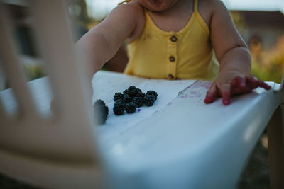 Midsection of baby girl with blackberries on table