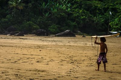 Full length of boy carrying surfboard at sandy beach