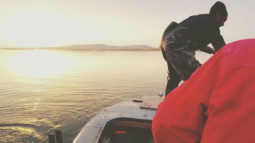 Rear view of woman by sea against sky during sunset