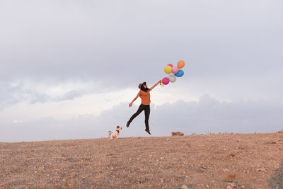 Full length of friends playing with balloons against sky