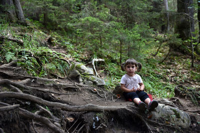 Cute toddler baby girl sitting on a tree trunk in the forest