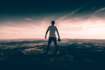 Rear view of man standing on rock against sky during sunset