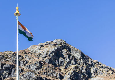 Low angle view of flag on mountain against clear blue sky