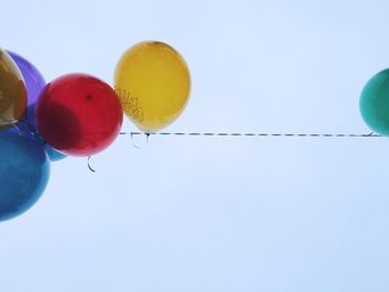 Low angle view of colorful balloons hanging from string against sky