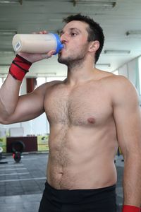 Shirtless muscular man drinking protein drink in gym