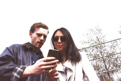Smiling young woman using smart phone against clear sky