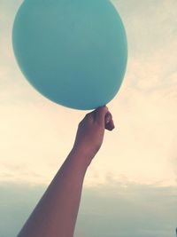 Close-up of hand holding ball with balloons against sky