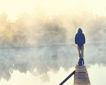 Rear view of man standing by lake against sky