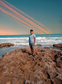 Full length of man standing on rock at beach against sky