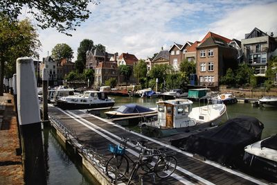 Boats moored in river by buildings against sky