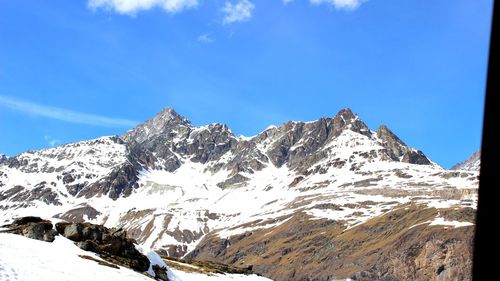 Low angle view of snowcapped mountains against blue sky