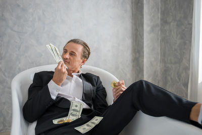 Businessman holding money while sitting against wall