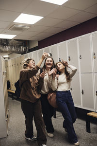 Happy teenage girl taking selfie with female friends while enjoying in school corridor