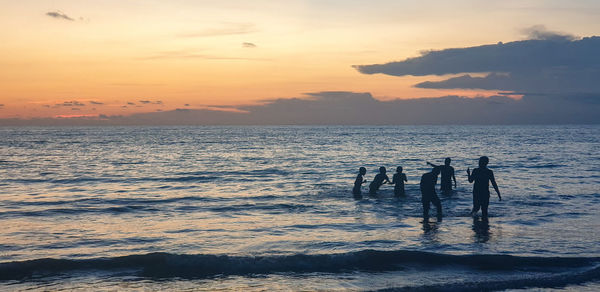 Silhouette people enjoying in sea against sky during sunset