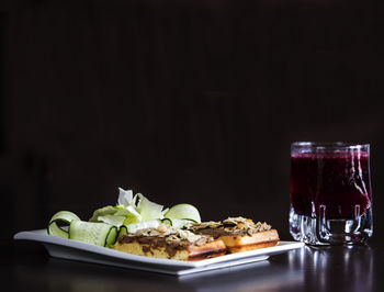 Close-up of belgian waffle served with almonds and cucumber in tray on black table