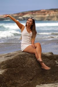 Full length of woman on rock at beach against sky