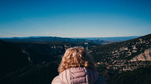 Rear view of woman standing on mountain against blue sky