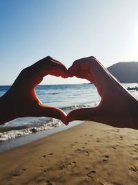 Hand holding heart shape on beach against sky