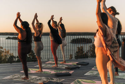 Female friends practicing tree pose together on patio at sunset