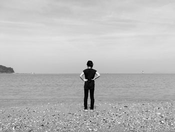 Rear view of woman standing at beach against sky