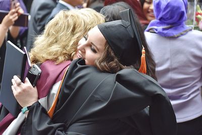 Friends in graduation gowns embracing while standing outdoors