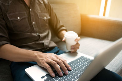 Midsection of woman using mobile phone while sitting on sofa at home