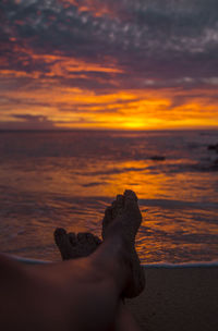 Low section of man on beach against sky during sunset