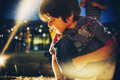 Digital composite image of boy crouching while playing outdoors at night