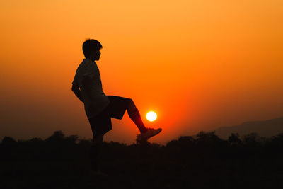 Silhouette man standing on field against orange sky