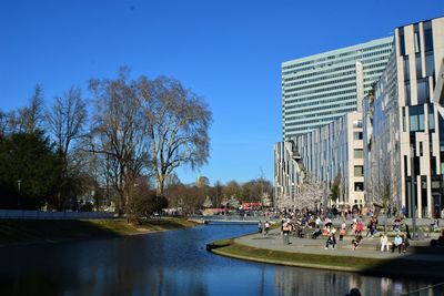 People on river by buildings against clear sky