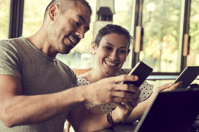 Smiling male showing smart phone to female partner in cafe