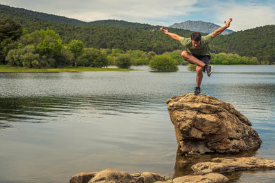 Man standing on rock by lake against sky