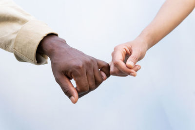 Crop unrecognizable diverse mam and woman holding hands with pinky grip against white background