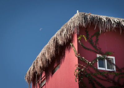 Low angle view of thatched roof of red house against sky with moon