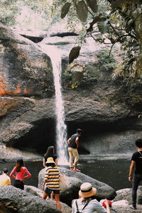 People sitting on rock against waterfall