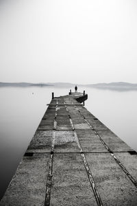 People sitting on pier over sea against clear sky