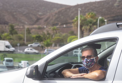 Portrait of smiling senior woman wearing flu mask sitting in car