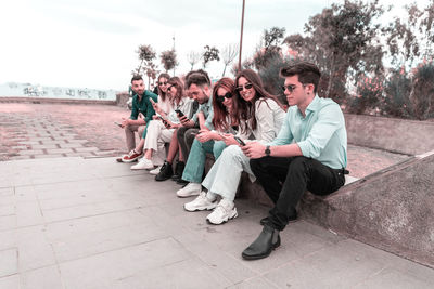 Group of friends using smart mobile phones app, sitting on a bench in a park - teenagers addiction 